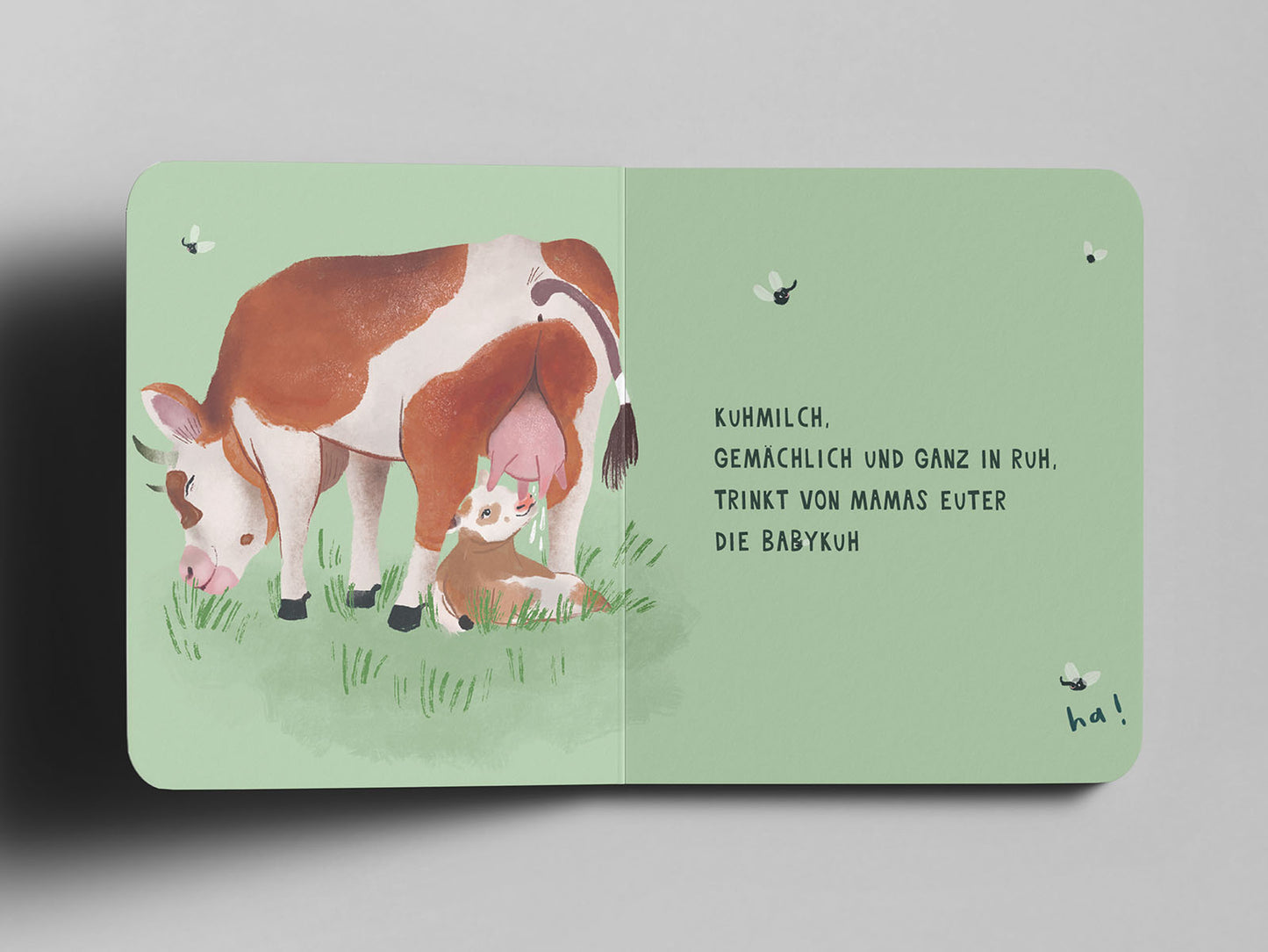 Aufgeschlagenes Pappbuch mit einer Illustration einer braun-weißen Kuh, die auf einer Wiese grast. Neben ihr trinkt ein Kälbchen Milch aus ihrem Euter. Drei kleine Fliegen schwirren umher. Auf der rechten Seite steht in schwarzer Schrift: ‚Kuhmilch, gemächlich und ganz in Ruh, trinkt von Mamas Euter die Babykuh‘. Unten rechts handschriftlich ergänzt: ‚ha!‘.