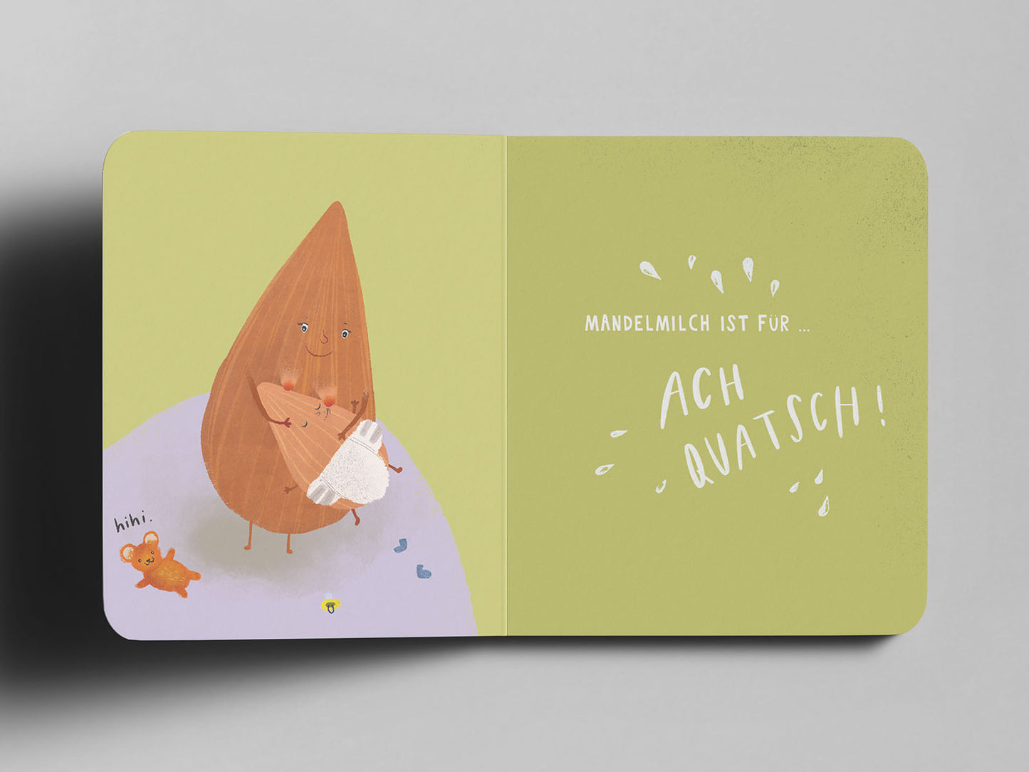 Aufgeschlagenes Pappbuch mit einer humorvollen Illustration: Eine große, lächelnde Mandel mit Armen und Beinen hält eine kleine Mandel mit Windel wie ein Baby im Arm. Links unten sitzt ein orangefarbener Teddybär mit dem handschriftlichen Text ‚hihi.‘ daneben. Auf der rechten Seite steht in weißer Schrift: Mandelmilch ist für … ACH QUATSCH!umgeben von kleinen Spritzern.