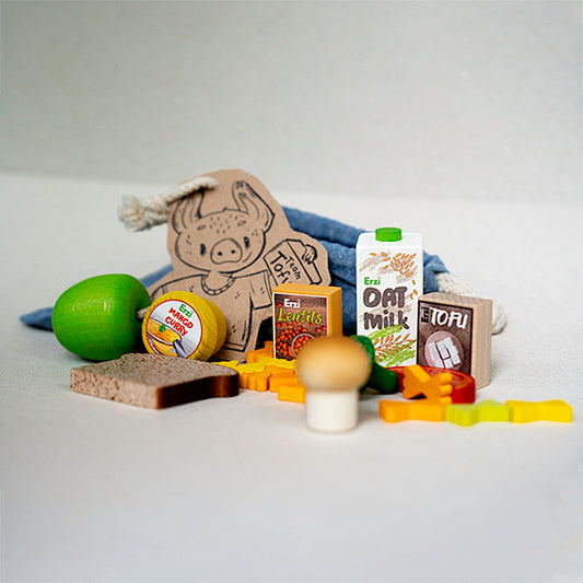 Kaufladen-Zubehör: Verschiedene vegane Lebensmittel aus Holz, liebevoll arrangiert rund um eine kleine blaue Stofftüte.