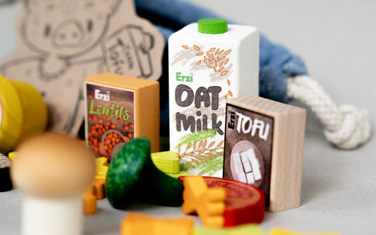 Kaufladen-Zubehör: Tofu, Hafermilch und Linsen aus Holz, liebevoll arrangiert rund um eine kleine blaue Stofftüte.
