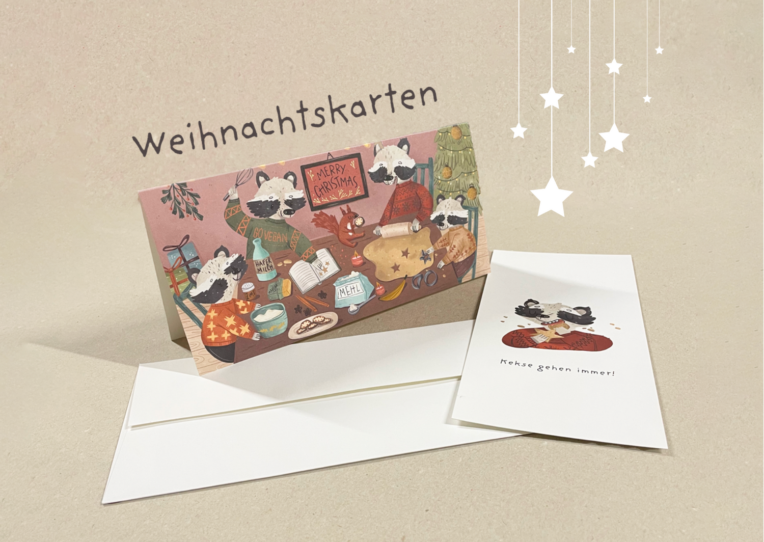 Weihnachtskarten-Set mit veganem Motiv. Die Hauptkarte zeigt eine gemütliche Szene mit Waschbären, die gemeinsam in einer weihnachtlichen Umgebung backen. Sie verwenden pflanzliche Zutaten wie Hafermilch und Mehl, während ein Schild mit der Aufschrift 'Merry Christmas' an der Wand hängt. Im Hintergrund steht ein geschmückter Weihnachtsbaum. Daneben liegt eine weitere Karte mit einem Waschbären, der Kekse isst, und dem Text 'Kekse gehen immer!'. 