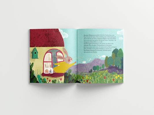Doppelseite aus dem illustrierten Kinderbuch 'Das blaue Ei'. Links im Bild schaut ein freundlicher Hase mit großen Ohren aus dem Fenster eines gemütlichen Hauses mit rotem Dach und gelber Fassade. Zwei Farbgläser mit Pinseln stehen auf der Fensterbank. Rechts erstreckt sich eine blühende Frühlingslandschaft mit grünen Wiesen, bunten Blumen, Bäumen und Bergen im Hintergrund. Der Himmel ist hellblau mit kleinen, weißen Wolken. Der Text auf der rechten Seite erzählt die Geschichte weiter.